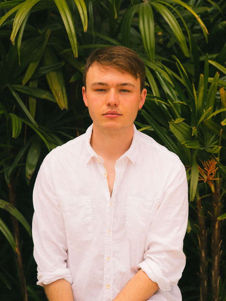 Man in white button-down shirt in front of tropical plants