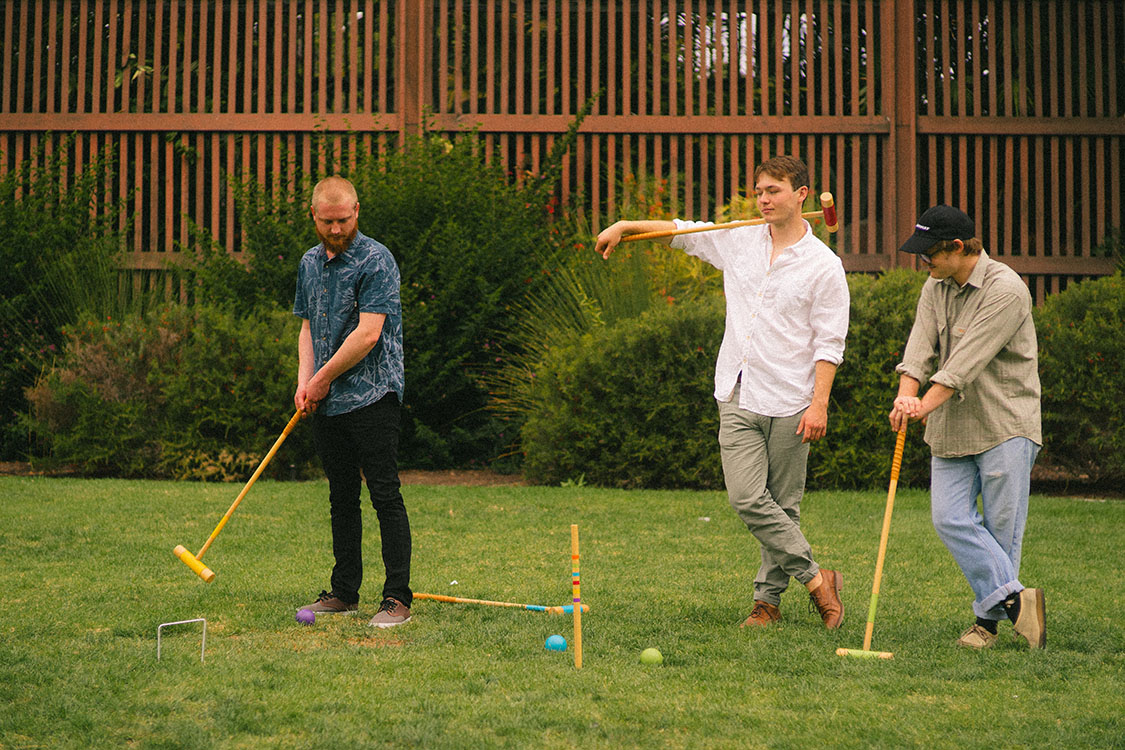 Three men play croquet in front of the Balboa Park Botanical Garden