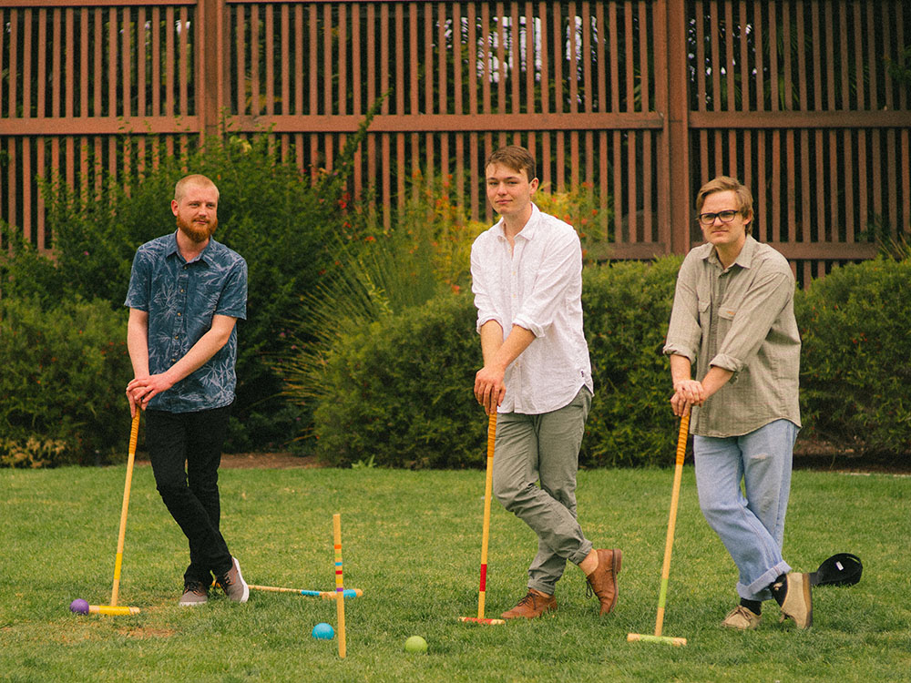 Three men play croquet in front of the Balboa Park Botanical Garden