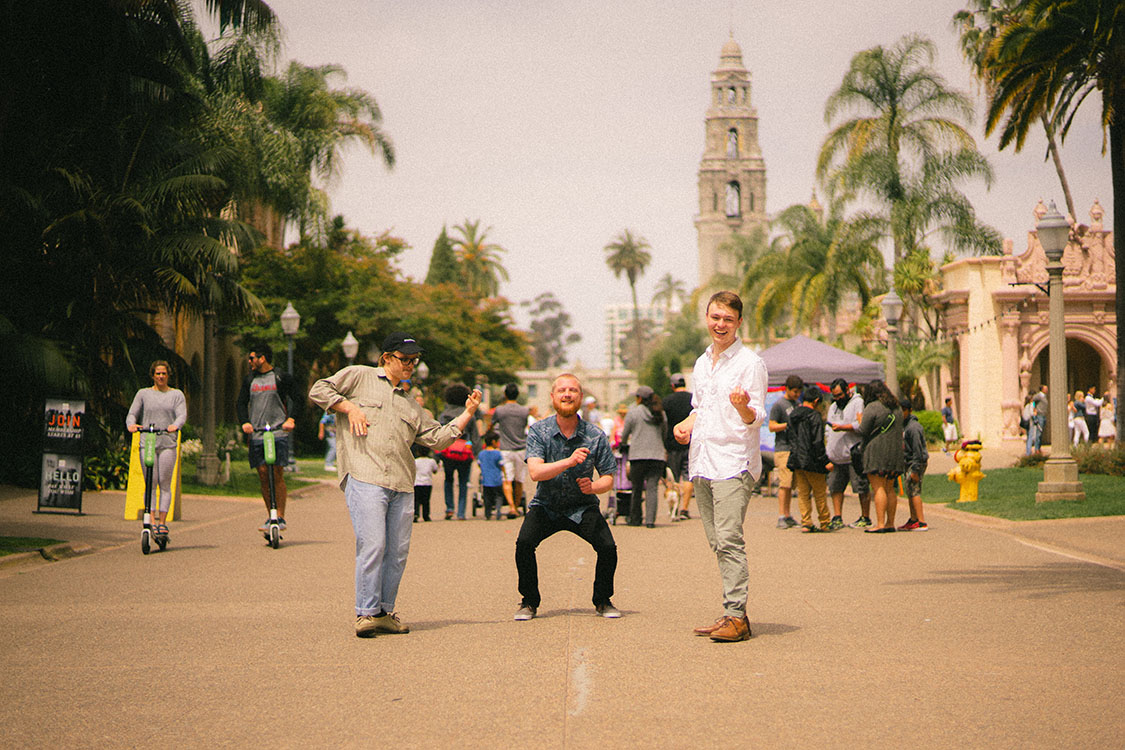 Three men play air instruments in Balboa Park